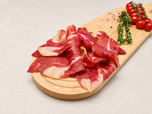 Tranches de jambon cru halal de bœuf sur une planche en bois, accompagnées de tomates cerises et de romarin.