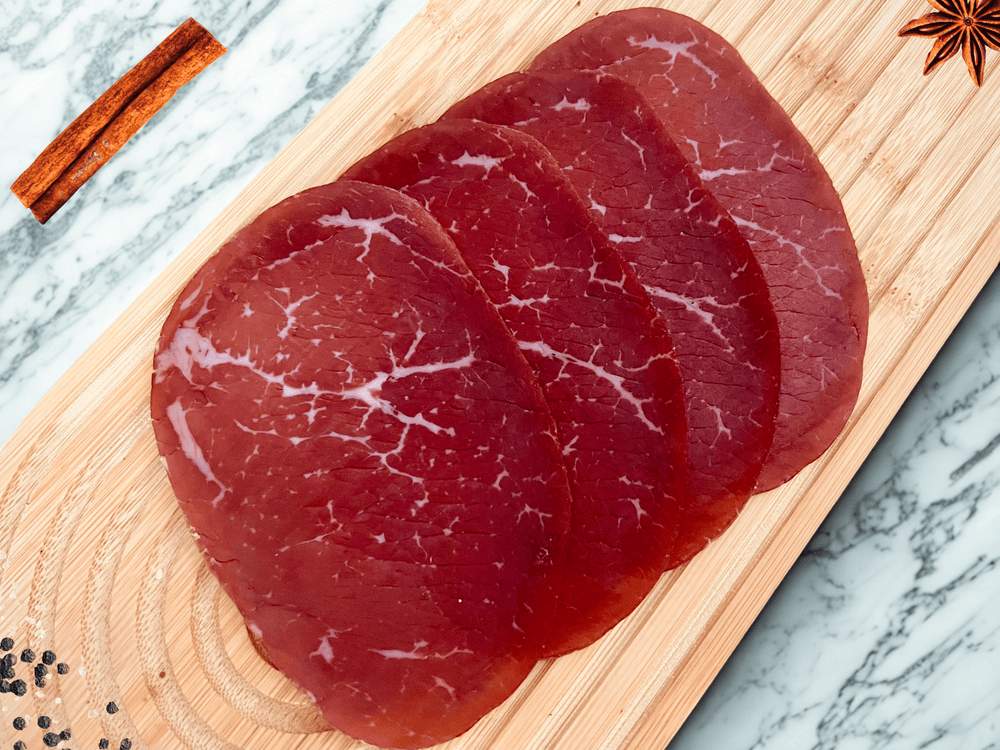 Tranches fines de bresaola de bœuf halal des Alpes italiennes présentées sur une planche en bois avec épices