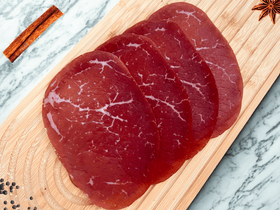 Tranches fines de bresaola de bœuf halal des Alpes italiennes présentées sur une planche en bois avec épices