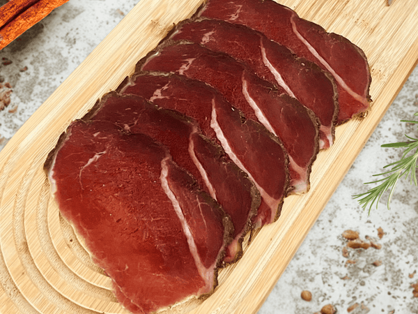 Tranches de noix de bœuf fumée halal Signature présentées sur une planche en bois avec herbes aromatiques