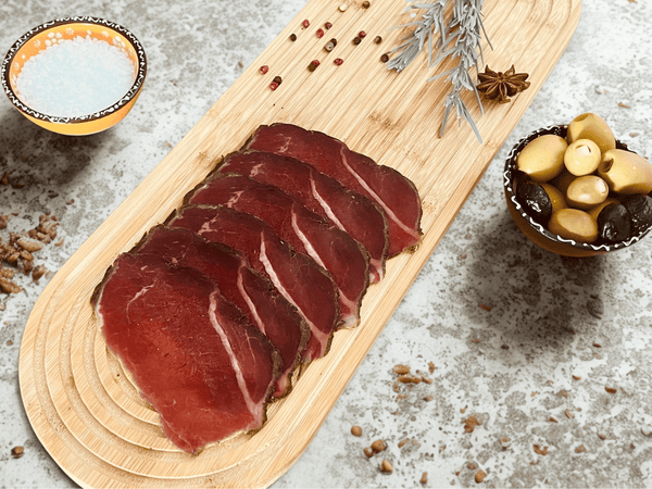 Tranches de noix de bœuf fumée halal Signature présentées sur une planche en bois avec olives, sel et épices
