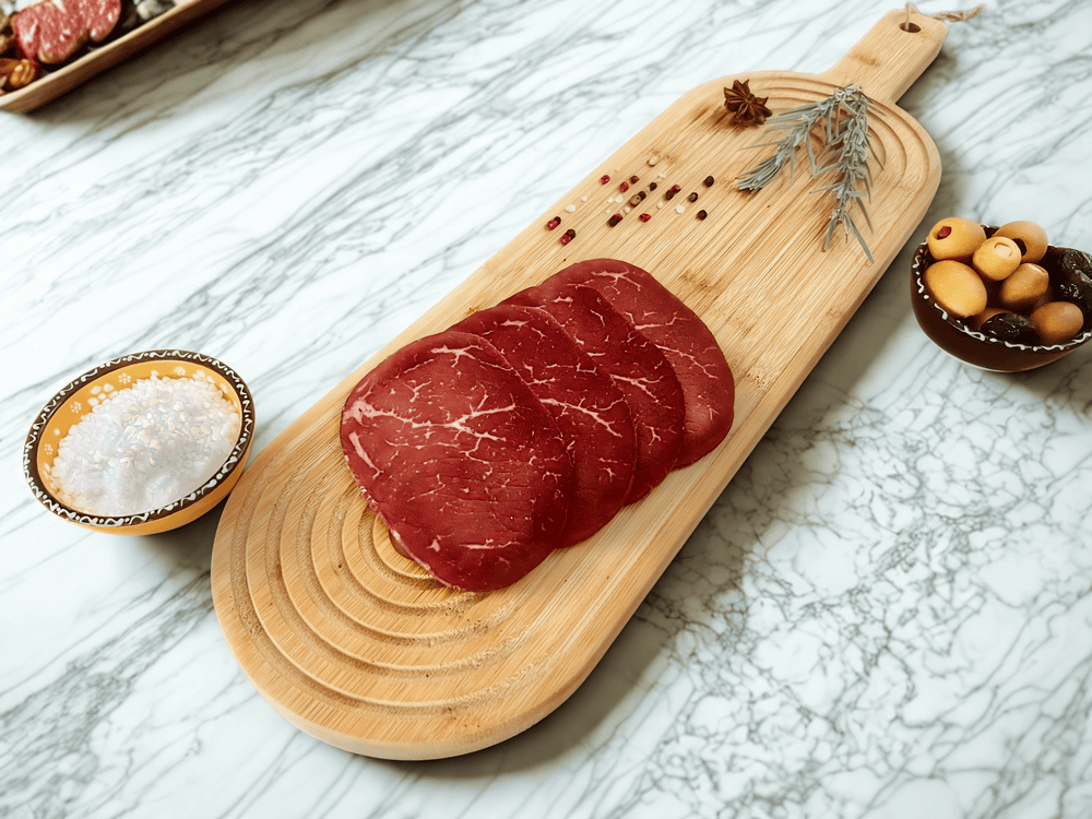 Tranches fines de bresaola de bœuf halal des Alpes italiennes présentées sur une planche en bois avec épices