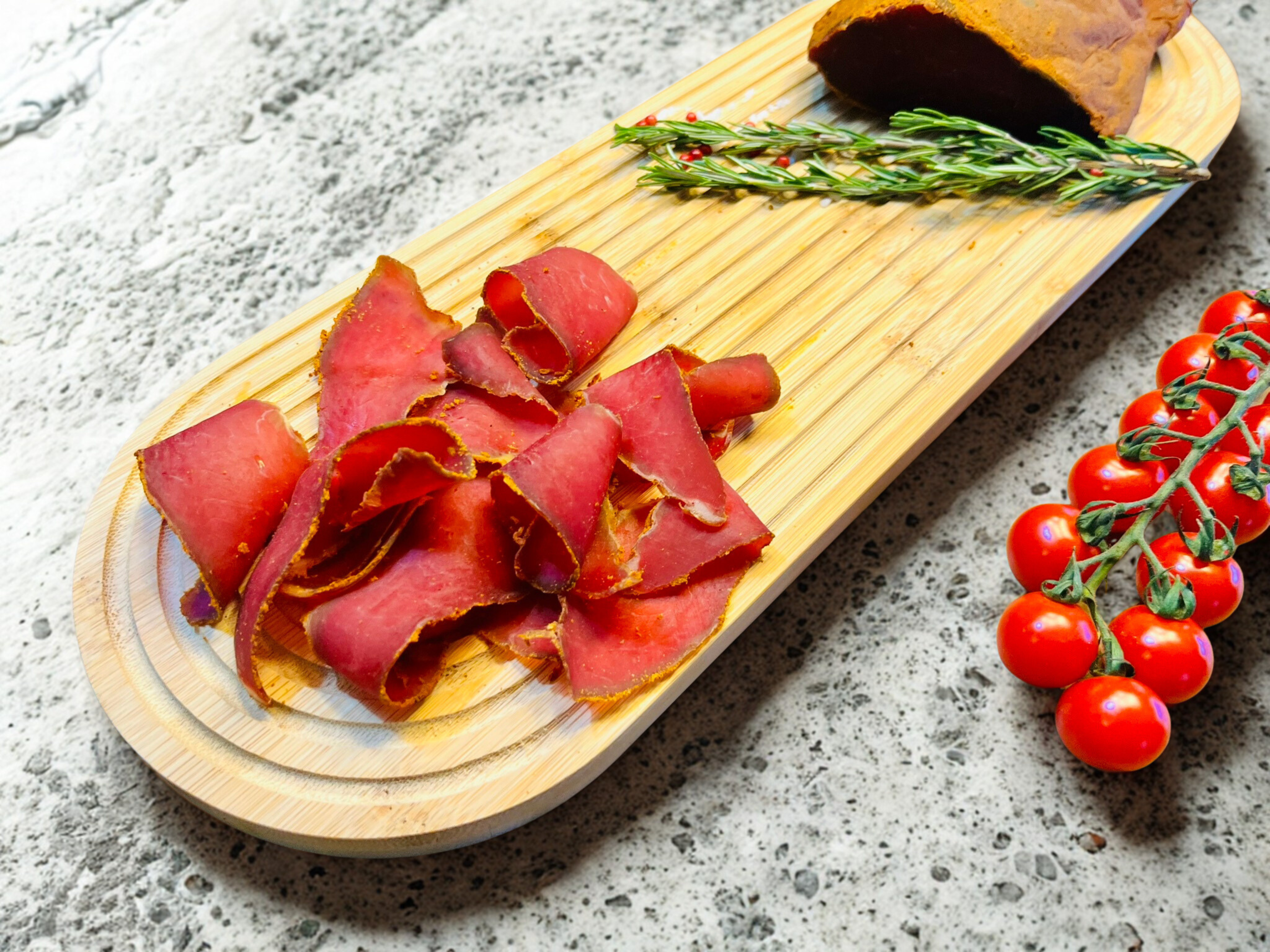 Pasterma ibérique de bœuf halal présentée sur plateau avec tomates cerises et romarin