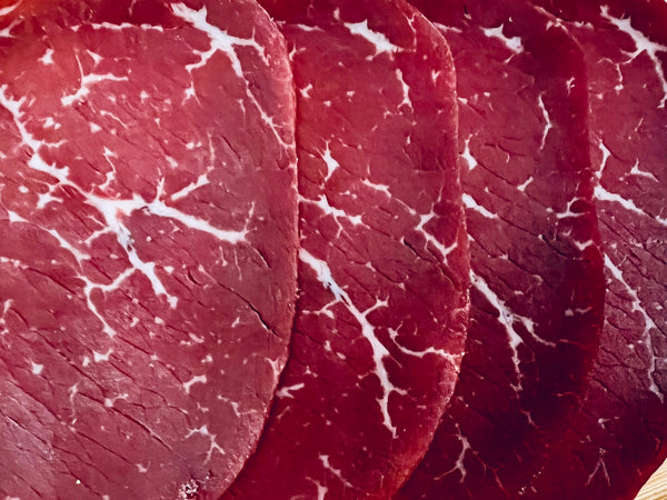 Gros plan de tranches fines de noix de bœuf séchée halal montrant le persillage naturel de la viande
